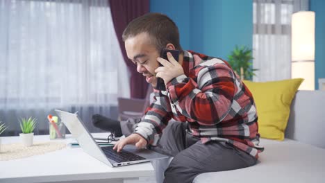 Happy-and-cheerful-dwarf-young-man-working-from-home-at-laptop-and-talking-on-phone.